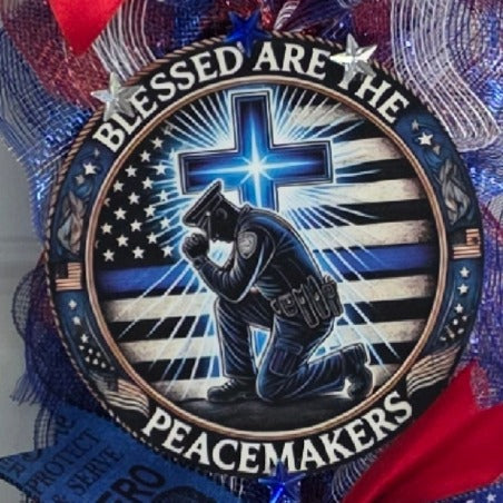 Close-up of Blessed Are The Peacemakers round center sign with kneeling officer and glowing cross on Thin Blue Line flag